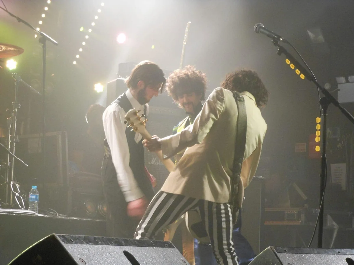 Stewart Vickers on stage in black tie beside the members of The Darkness